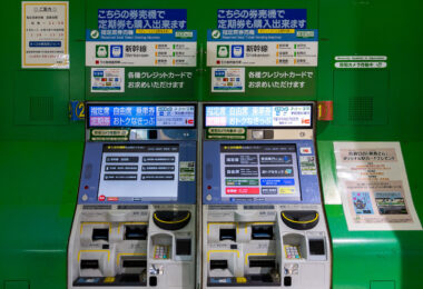 A pair of Shinkansen ticket vending machines at a Japanese railway station, featuring multilingual touchscreens and payment slots for both cash and IC cards. These machines allow travelers to purchase reserved and non-reserved tickets for Japan’s high-speed rail network, as well as commuter passes and regional fare cards. The bright green backdrop and clear signage reflect Japan Rail’s emphasis on efficiency and accessibility, enabling quick transactions even during the busiest travel hours.