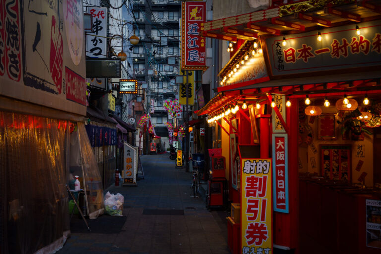 Shinsekai, Osaka: Illuminated Restaurants and Signs at Dusk 1 Illuminated restaurants and signs line a narrow street in Shinsekai, Osaka, Japan, at dusk. The area is known for its retro atmosphere and entertainment.