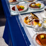 A display of shokuhin sampuru—hyper-realistic plastic food models—outside a café in Osaka. These handcrafted replicas have been a fixture of Japanese dining culture since the early 20th century, originally created to help restaurants communicate menu items to customers at a time when Western dishes were still unfamiliar to many diners.

The models shown here include classic café desserts such as pancakes, pudding, and parfait toppings, each sealed in protective cases to preserve their lacquered shine. Osaka remains one of the country’s major production centers for sampuru, where artisans still sculpt and paint many pieces by hand to ensure the lifelike detail that continues to define this uniquely Japanese craft.