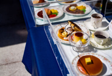 A display of shokuhin sampuru—hyper-realistic plastic food models—outside a café in Osaka. These handcrafted replicas have been a fixture of Japanese dining culture since the early 20th century, originally created to help restaurants communicate menu items to customers at a time when Western dishes were still unfamiliar to many diners.

The models shown here include classic café desserts such as pancakes, pudding, and parfait toppings, each sealed in protective cases to preserve their lacquered shine. Osaka remains one of the country’s major production centers for sampuru, where artisans still sculpt and paint many pieces by hand to ensure the lifelike detail that continues to define this uniquely Japanese craft.