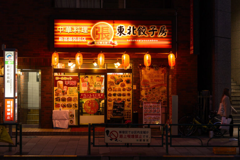 Tohoku Gyozabou Near Shinjuku Gyoen 2 Tohoku Gyozabou, located just east of Shinjuku Gyoen National Garden, is one of many small neighborhood restaurants that serve the area’s mix of office workers, residents, and visitors. Spots like this are common throughout Shinjuku’s quieter side streets, offering regional Chinese-style dishes and set meals late into the evening, contrasting with the larger entertainment corridors to the west around Shinjuku Station and Kabukichō.
The surrounding district developed after World War II as Shinjuku expanded outward from the rail hub, creating a network of narrow commercial blocks filled with independent eateries. Many of these restaurants continue to display brightly illuminated exterior menus and lantern signage, part of the city’s longstanding street-level food culture that encourages casual walk-in dining.