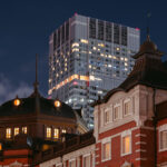 The historic Marunouchi side of Tokyo Station glows warmly at dusk, its red-brick exterior and copper domes standing in contrast to the modern skyscrapers of the surrounding Marunouchi business district. Opened in 1914 and designed by architect Tatsuno Kingo, the station served as the central gateway for Japan’s expanding rail network during the early 20th century.

The dramatic juxtaposition in this March 2023 photograph highlights more than a century of architectural evolution: the restored station building—meticulously reconstructed after wartime damage—foregrounds the sleek high-rise towers that define contemporary central Tokyo. Together, they illustrate how Tokyo layers historic preservation and modern development within one of the busiest transport hubs in the world.