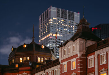 The historic Marunouchi side of Tokyo Station glows warmly at dusk, its red-brick exterior and copper domes standing in contrast to the modern skyscrapers of the surrounding Marunouchi business district. Opened in 1914 and designed by architect Tatsuno Kingo, the station served as the central gateway for Japan’s expanding rail network during the early 20th century.

The dramatic juxtaposition in this March 2023 photograph highlights more than a century of architectural evolution: the restored station building—meticulously reconstructed after wartime damage—foregrounds the sleek high-rise towers that define contemporary central Tokyo. Together, they illustrate how Tokyo layers historic preservation and modern development within one of the busiest transport hubs in the world.
