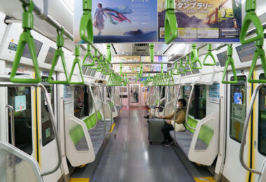 An interior view of a JR East E235 series train on the Yamanote Line, photographed in March 2023. Introduced beginning in 2015, the E235 fleet modernized one of Tokyo’s busiest rail corridors with full-width LCD displays, energy-efficient systems, and redesigned seating meant to improve passenger flow during peak congestion.

The Yamanote Line has operated as Tokyo’s central loop since 1925, linking major districts such as Shinjuku, Shibuya, Ueno, and Tokyo Station. Its frequent headways—often under three minutes—make it a fundamental component of the city’s rail network.

In this off-peak moment, the largely empty car highlights features typical of contemporary JR East design: bright color-coded grab handles, platform-screen door alignment, and extensive in-car advertising screens catering to both commuters and visitors navigating the metropolitan loop.