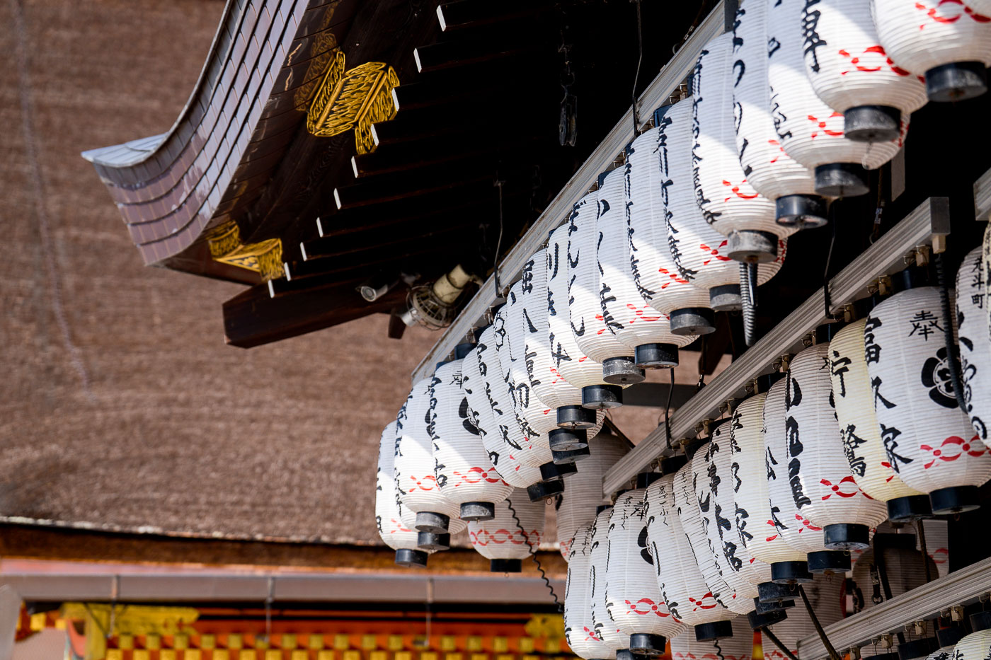 White paper lanterns with Japanese characters hang under the eaves of Yasaka Shrine in Kyoto, Japan.