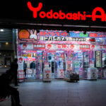 Yodobashi-Akiba, photographed in March 2023, is one of Tokyo’s largest electronics retail complexes and a major landmark in the Akihabara district. Opened in 2005 as part of a wider redevelopment effort around JR Akihabara Station, the multi-story store consolidated several specialty floors—computers, cameras, gaming, home appliances, musical instruments—into a single destination that helped redefine the area’s retail identity in the 2000s.

Its brightly illuminated entrance, typically covered in seasonal and promotional signage, reflects the competitive electronics market that shaped modern Akihabara. The building also connects directly to the Tsukuba Express line and sits beside the redevelopment zone that transformed the district from its postwar reputation as “Electric Town” into a mix of technology retail, office towers, and entertainment venues.