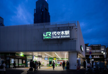 As dusk settles over Shibuya, the illuminated sign of Yoyogi Station (代々木駅) glows against a deep indigo sky, marking one of Tokyo’s key JR East commuter hubs. Opened in 1906, Yoyogi serves both the Yamanote and Chuo-Sobu lines, connecting thousands of travelers daily between Shinjuku and Harajuku. The cool blue hour lighting highlights the crisp white façade and the green JR branding, captured here with a balanced exposure to preserve both architectural detail and ambient light reflections. Taken in early evening with a 35mm f/1.8 lens, this frame emphasizes the quiet rhythm of Tokyo’s rush hour just before nightfall.