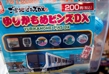 A souvenir capsule vending machine featuring “Yurikamome Pins DX” collectibles, themed after the Yurikamome Line—Tokyo’s automated, elevated transit system linking Shimbashi with the waterfront district of Toyosu via Odaiba. The pin set celebrates key stations and landmarks along the route, such as Fuji Television, Rainbow Bridge, and Tokyo Big Sight, reflecting the line’s blend of technology and tourism appeal.

Opened in 1995, the Yurikamome Line was Japan’s first fully automated guideway transit system, operating without onboard drivers. It was conceived to connect Tokyo’s redeveloped bayside area with the city center, helping transform Odaiba from a reclaimed industrial zone into a futuristic entertainment and business hub. Its name, “Yurikamome,” comes from the black-headed gull native to Tokyo Bay—a fitting emblem for this sleek, seafront line.