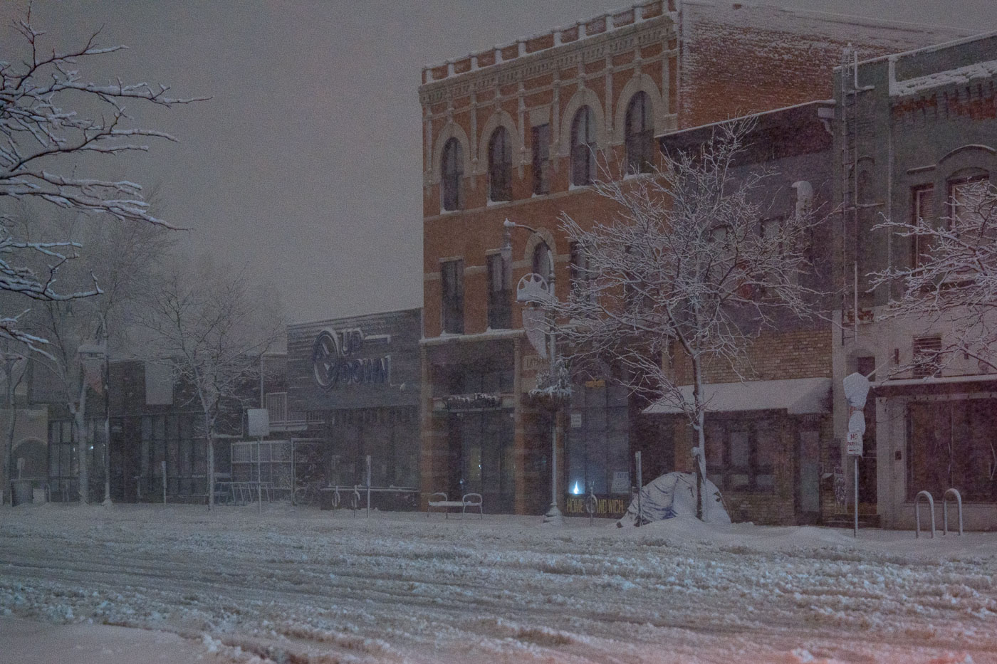 Buildings line Nicollet Avenue in Minneapolis during an April blizzard, with signs for "UP-DOWN" and "HOME SANDWICH" visible.