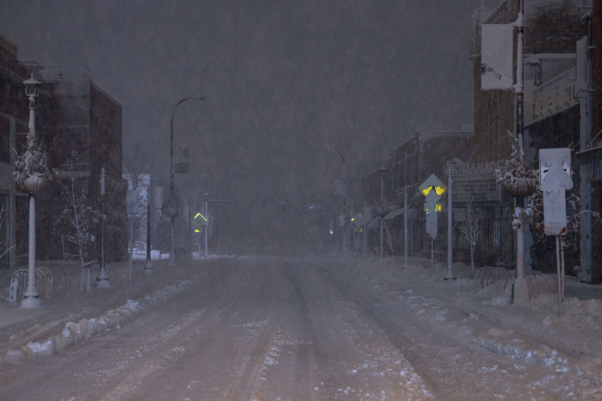 Minneapolis street during an April 2023 blizzard, with snow covering roads and sidewalks. Traffic lights and signs are visible through the falling snow.