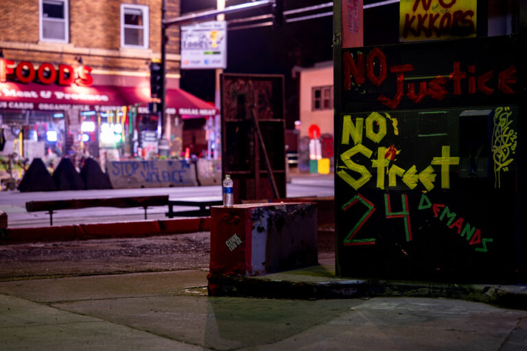 George Floyd Square: 24 Demands at The People's Way 3 The intersection of 38th Street and Chicago Avenue in Minneapolis, known as George Floyd Square or The People's Way, became a focal point of protest following the murder of George Floyd on May 25, 2020. The area was occupied by activists and community members for an extended period, serving as a space for remembrance, activism, and community organizing. Signs and barricades, such as those visible in the photograph, marked the perimeter and communicated messages related to justice and the group's demands.