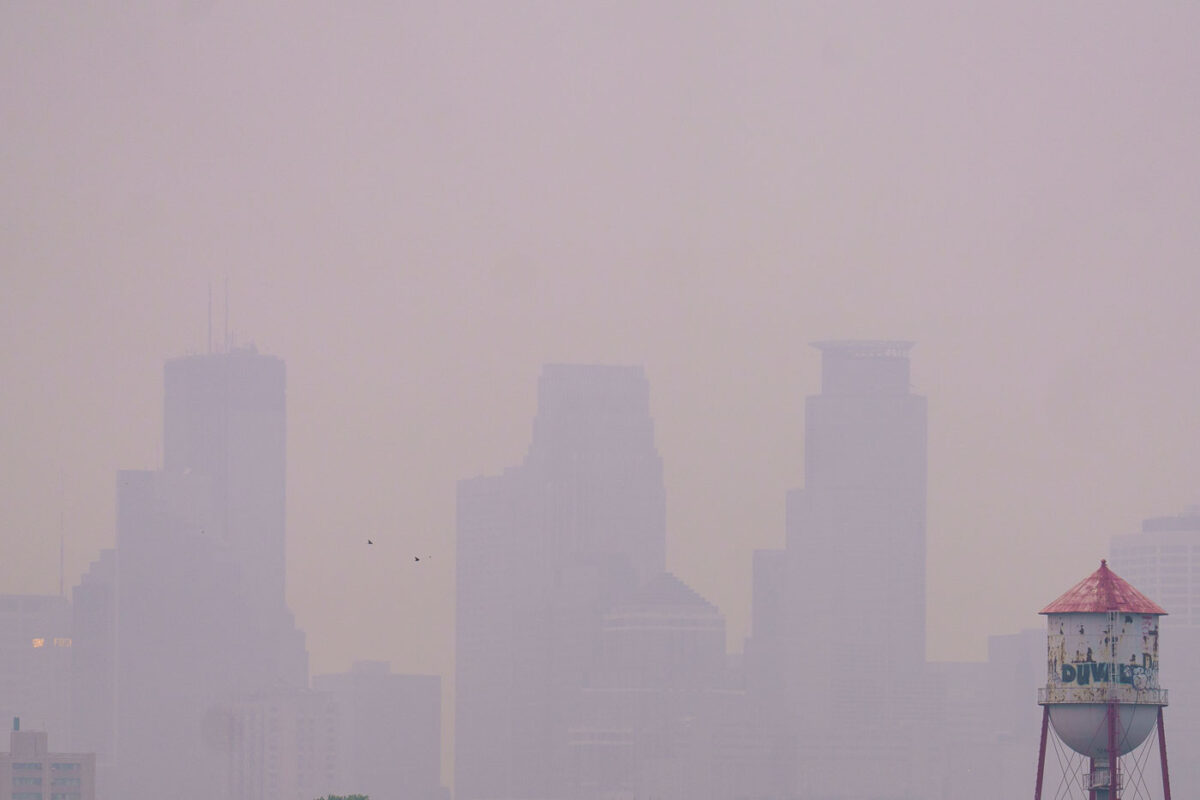 Wildfire smoke from Canada drifts into Minneapolis, significantly reducing visibility of the downtown skyline. The smoke, a result of widespread wildfires, impacted air quality across the region. The image also shows a water tower, a common feature in urban environments providing essential water storage and pressure for municipal systems.