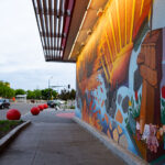 A mural depicting the George Floyd Square fists with the burned out Minneapolis third precinct building in the background. The mural is at the entrance of the rebuilt Target Store.