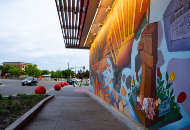 A mural depicting the George Floyd Square fists with the burned out Minneapolis third precinct building in the background. The mural is at the entrance of the rebuilt Target Store.