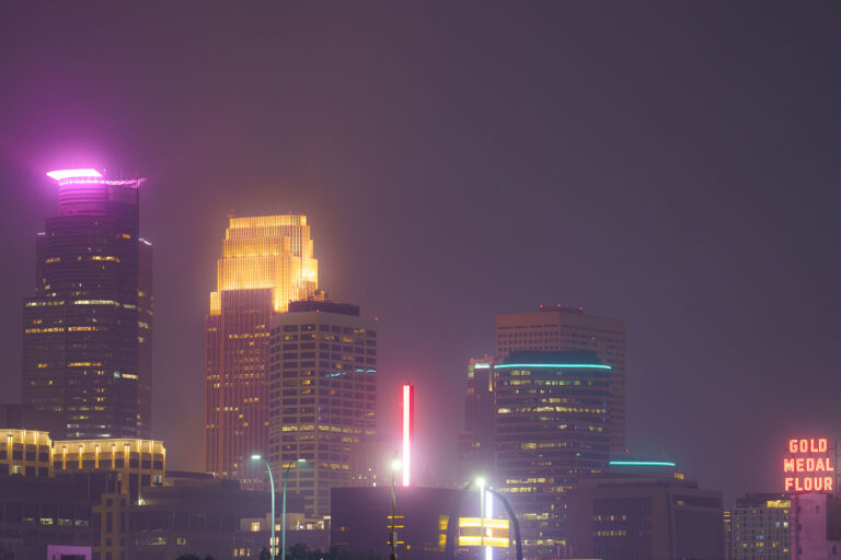 Minneapolis Skyline Under Wildfire Smoke Haze 2 The Minneapolis city skyline is obscured by haze from Canadian wildfires, impacting air quality across the region. The "Gold Medal Flour" sign, a historic landmark dating back to the early 20th century, is visible through the atmospheric conditions. This event highlights the increasing frequency of such air quality alerts due to climate change and widespread wildfires. The city's downtown core, with its mix of modern skyscrapers and older structures, serves as the economic and cultural hub of Minnesota.