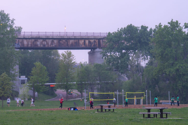 Volleyball near Mississippi River Bridge, Minneapolis 1 Despite air quality warnings issued due to wildfire smoke, residents engaged in outdoor activities, including volleyball, near the Mississippi River in Minneapolis. The elevated structure in the background is a railway bridge, a vital piece of transportation infrastructure that has served the city for decades. The presence of people enjoying the park highlights the resilience of community life even amidst environmental concerns.