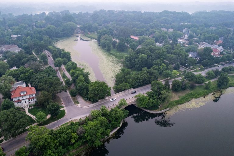 Canadian Wildfire Smoke Over Lake of the Isles, Minneapolis 1 Aerial view of a residential neighborhood with a river running through tree-covered terrain under hazy conditions.