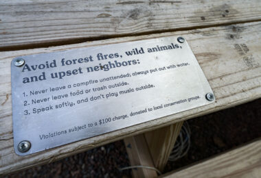 A notice on a picnic table at a Getaway campground in Kettle River. "Avoid forest fires, wild animals, and upset neighbors: 1. Never leave a campfire unattended; always put out the water. 2. Never leave food or trash outside. 3. Speak softly, and don't play music outside.