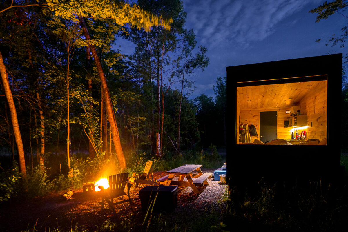 A modern cabin and campfire are lit at dusk near the Kettle River