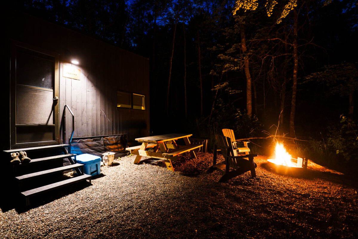 A cabin labeled "JAUNITA" is lit at night beside a campfire near the Kettle River