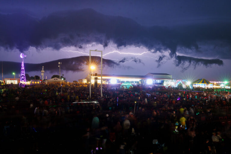 Lightning Strikes Over Rock Fest Crowd in Cadott, Wisconsin 1 Lightning illuminates the sky over a large crowd attending Rock Fest in Cadott, Wisconsin. This annual music festival, held at the Cadott Fairgrounds, draws thousands of attendees for multiple days of rock and heavy metal performances. The event has a long history, dating back to 1994, and has become a significant cultural gathering for fans of the genre in the Midwest. The image captures a moment of natural spectacle interrupting the planned entertainment, highlighting the unpredictable elements that can affect large outdoor events.