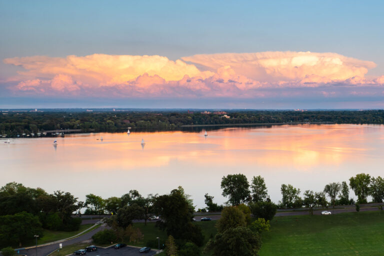 Bde Maka Ska Lake Sunset Clouds Minneapolis 1 Sunset clouds over Bde Maka Ska Lake in Minneapolis, Minnesota, with sailboats on the water and trees lining the shore.