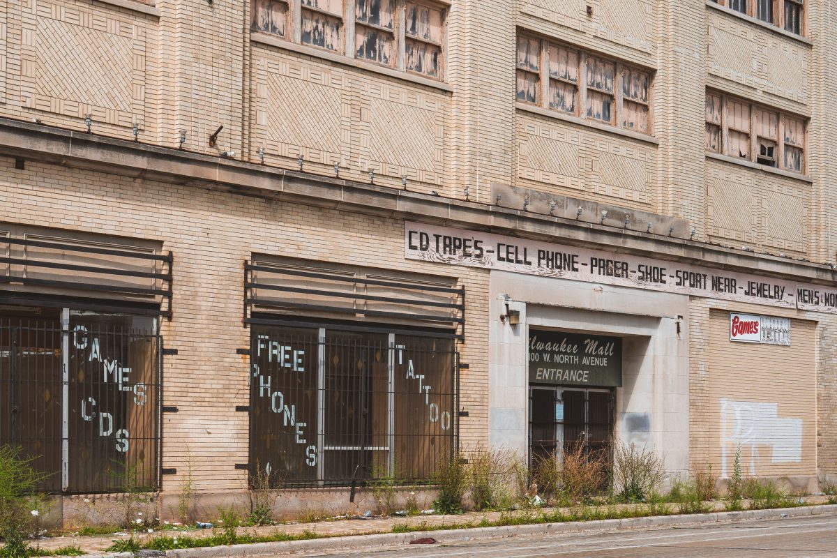 Abandoned storefront of Milwaukee Mall with boarded windows and faded signage on brick facade.