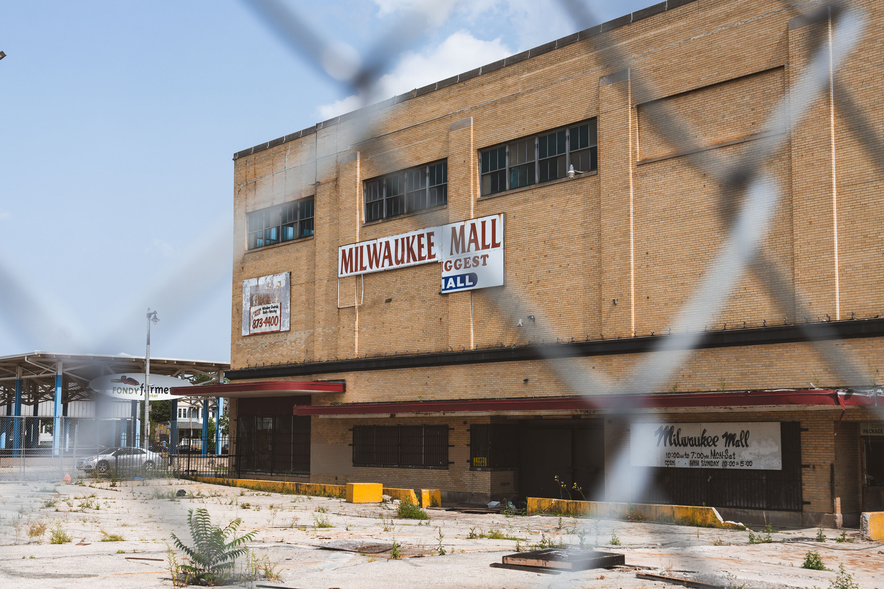 The abandoned Milwaukee Mall building in Wisconsin stands vacant with boarded windows and overgrown pavement.