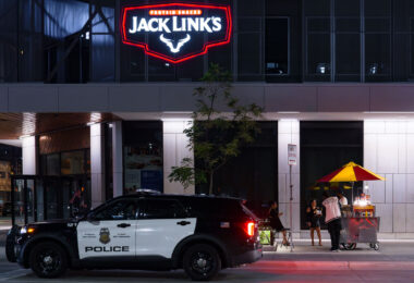 People stand at a food stand on Hennepin Avenue in downtown Minneapolis as a Minneapolis police squad car drives by.