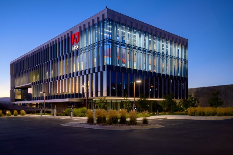 Adobe's modern office building in Lehi, Utah illuminated at dusk with vertical metal louvers and landscaping.