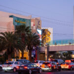 The MGM Grand stands as one of the most iconic landmarks on the Las Vegas Strip, instantly recognizable by its emerald-green lighting and massive golden lion statue at the entrance. Opened in 1993, it remains one of the largest hotels in the world, housing over 6,800 rooms, a sprawling casino, and major entertainment venues. The resort is home to Hakkasan nightclub and has hosted countless concerts, boxing matches, and celebrity residencies over the years. In this scene, evening traffic and palm trees frame the grand façade, capturing the constant motion and energy that define this busy corner of Las Vegas Boulevard.