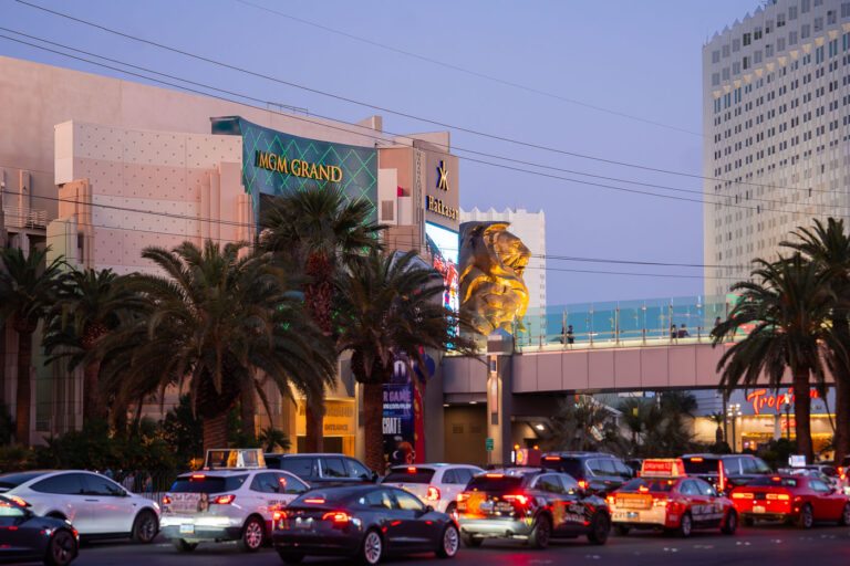 MGM Grand Lion in Las Vegas 2 The MGM Grand stands as one of the most iconic landmarks on the Las Vegas Strip, instantly recognizable by its emerald-green lighting and massive golden lion statue at the entrance. Opened in 1993, it remains one of the largest hotels in the world, housing over 6,800 rooms, a sprawling casino, and major entertainment venues. The resort is home to Hakkasan nightclub and has hosted countless concerts, boxing matches, and celebrity residencies over the years. In this scene, evening traffic and palm trees frame the grand façade, capturing the constant motion and energy that define this busy corner of Las Vegas Boulevard.