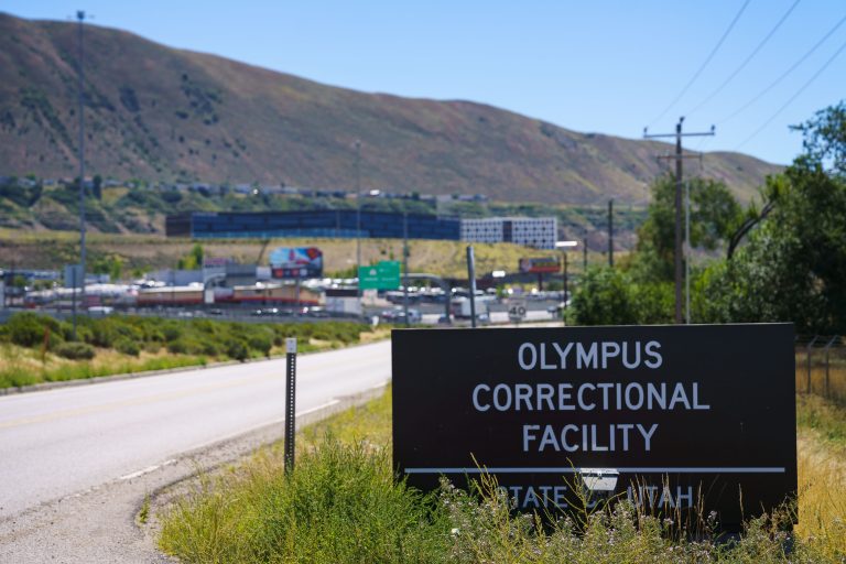 Olympus Correctional Facility sign in Draper, Utah, with the prison complex visible beyond.