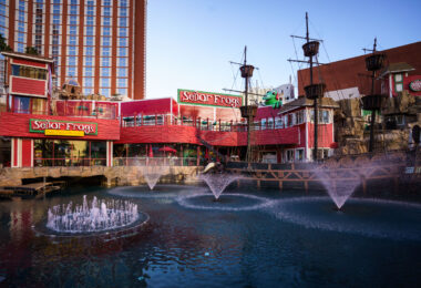 The waterfront at Treasure Island features Señor Frog’s, a lively restaurant and bar that overlooks the resort’s lagoon and replica pirate ships. Once home to the “Sirens of TI” show, the area now serves as a social hub with fountains, themed décor, and outdoor seating that captures views of the Las Vegas Strip. The playful red exterior and nautical props recall the property’s original pirate theme, blending nostalgia with the casual, party-friendly energy that defines this corner of the Strip today.