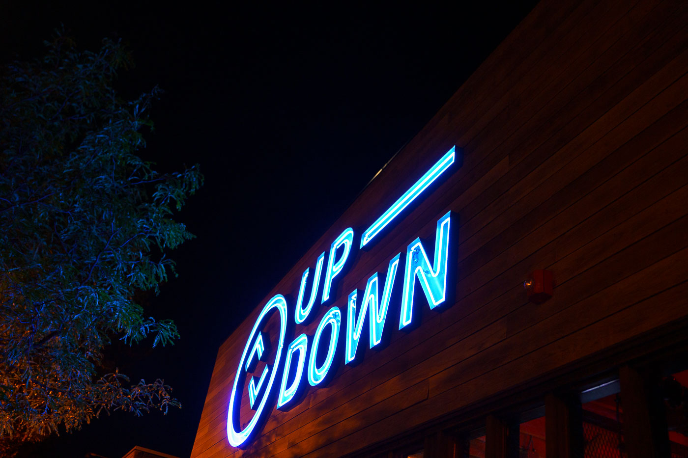 A blue neon sign for the UP-DOWN bar glows on a wooden facade on Lyndale Avenue in Minneapolis, September 2023.