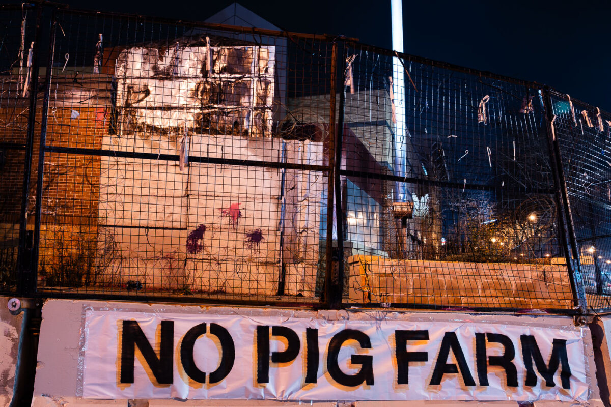 A banner reading "NO PIG FARM" on a barricade around the former Minneapolis police third precinct. The building was burned in the 2020 Uprising following the murder of George Floyd. It's sat vacant ever since. November 2023.