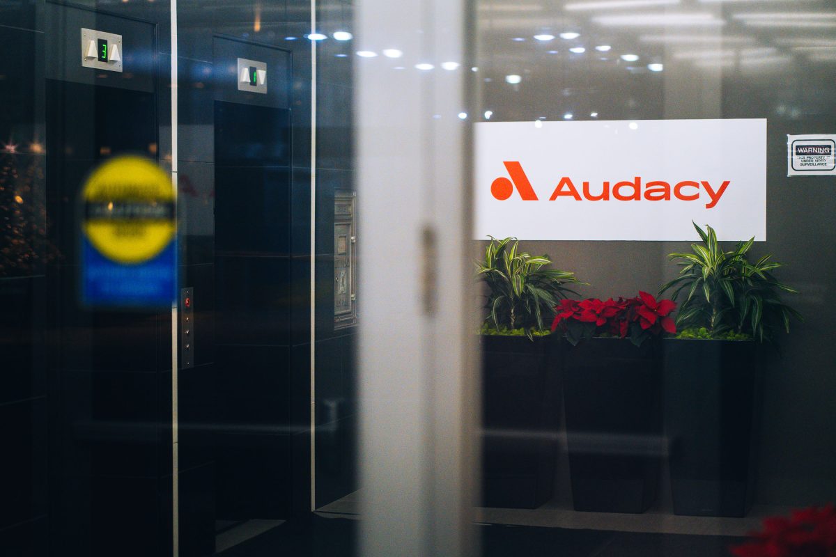 Audacy office entrance in downtown Minneapolis displays the company's illuminated logo above potted plants.