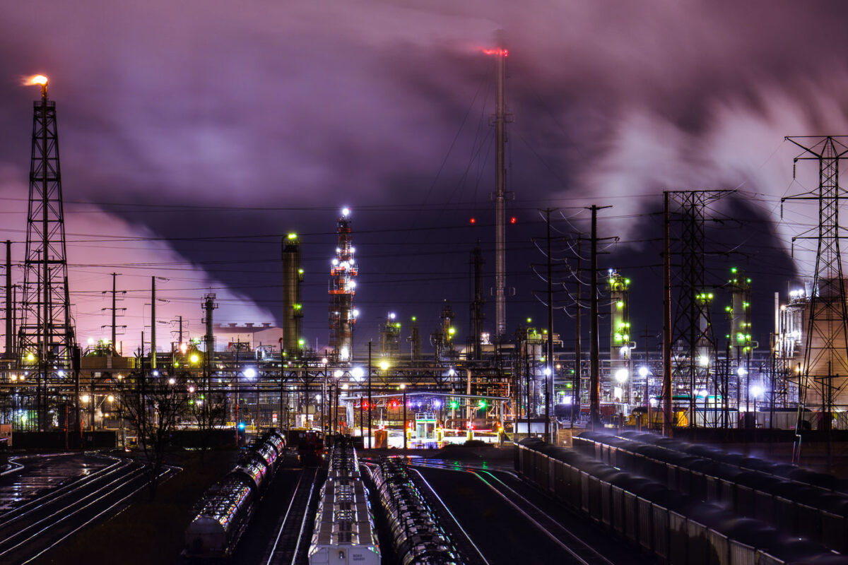 The BP Whiting Refinery in Indiana, the Midwest's largest oil refinery, is illuminated at night with a flare stack burning and steam rising.