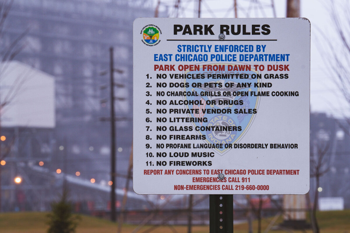 Park rules sign in Marktown, East Chicago, Indiana, lists regulations enforced by the East Chicago Police Department, including prohibitions on vehicles on grass, pets, alcohol, and firearms.
