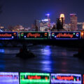 Lit up holiday train crosses river with skyline