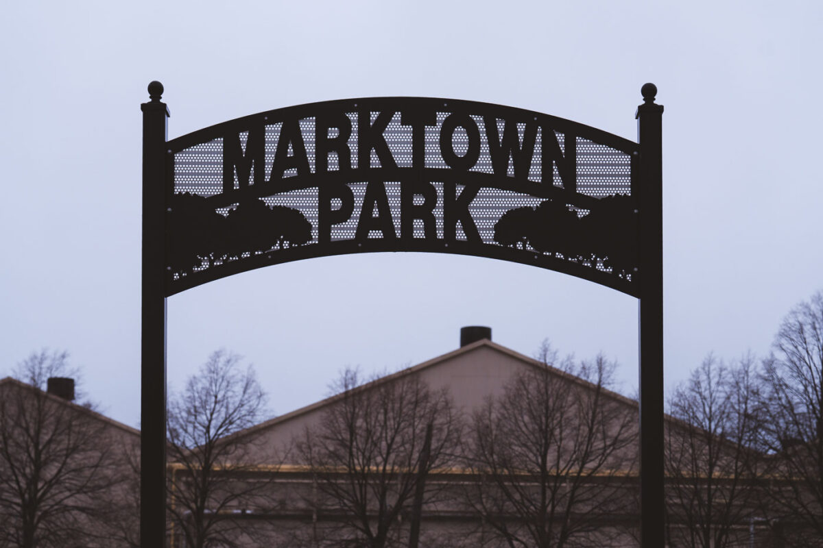 Marktown Park entrance sign in East Chicago, Indiana, a historic company town. The black metal archway sign features perforated text and silhouetted trees.