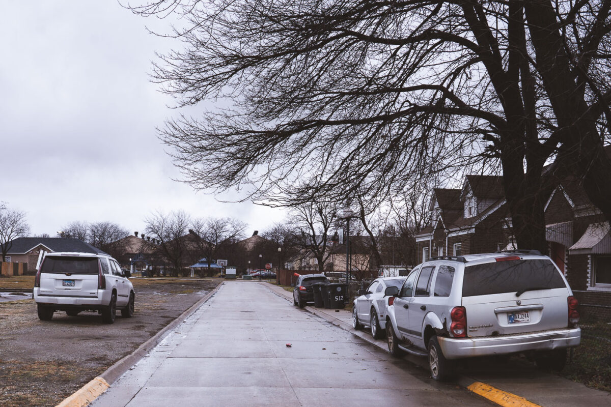 Park Street in Marktown, Indiana, a historic company town, shows residential housing and parked vehicles under a cloudy sky.