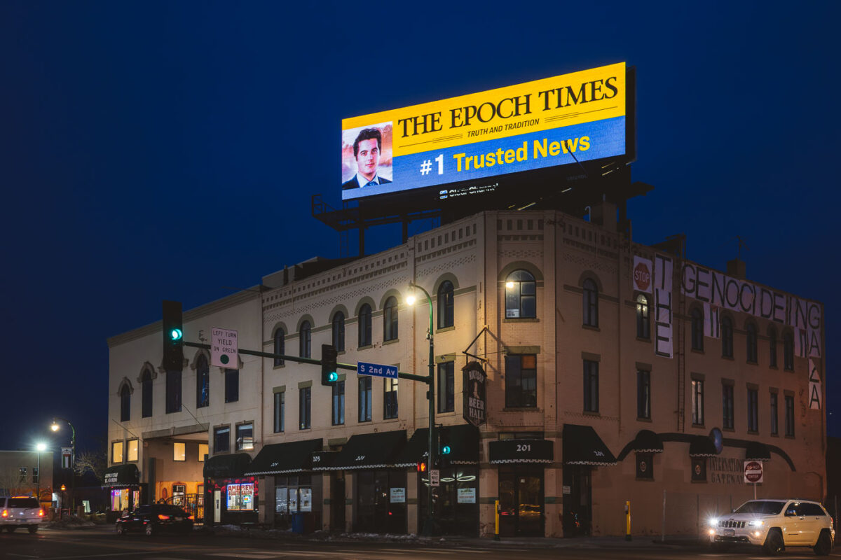 An Epoch Times billboard over a building at Lake Street and 2nd Ave. On the other side is protest banners reading "Stop the genocide in Gaza".