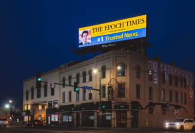 An Epoch Times billboard over a building at Lake Street and 2nd Ave. On the other side is protest banners reading "Stop the genocide in Gaza".