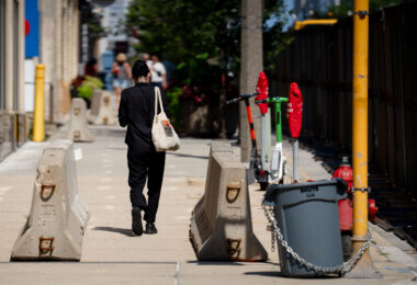 A woman walks down the sidewalk that's filled with concrete barriers and security fencing near the Pfister Hotel.