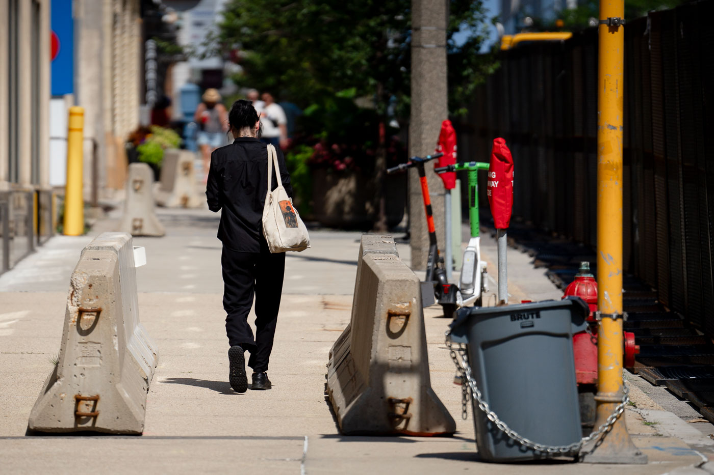 A woman walks down the sidewalk that's filled with concrete barriers and security fencing near the Pfister Hotel.