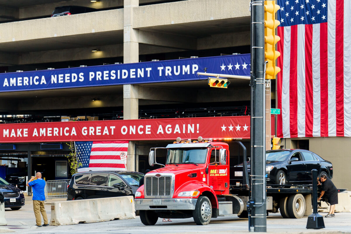 A car being towed near a parking ramp at the 2024 Republican National Convention. The ramp is wrapped with Make America Great Again branding.