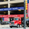 A car being towed near a parking ramp at the 2024 Republican National Convention. The ramp is wrapped with Make America Great Again branding.