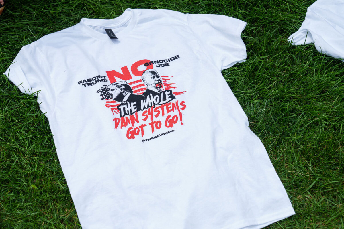 A t-shirt in the grass at the 2024 Republican National Convention. It reads No Genocide Joe No Fascist Trump. The whole damn system's got to go! Shirt from The Revolutionary Communist Party.
