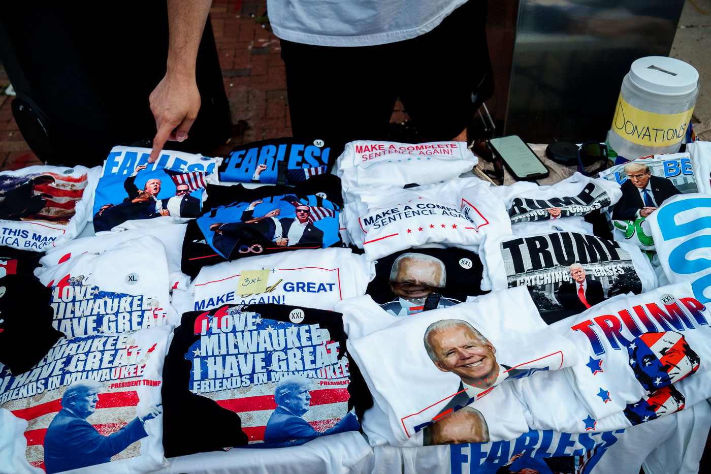 A T-shirt vendor at the Republican National Convention. Pointing to what he says is his best selling shirt, one of after Trump was shot.